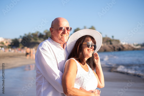 Happy bonding senior couple hugging on the seashore face the sunset enjoying vacation and retirement, two smiling people expressing love and tenderness