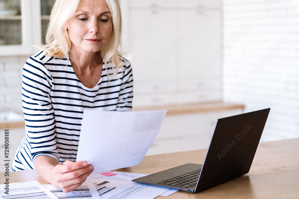 Middle aged female enterpreneur working at home, reading paper documents Middle aged female enterpreneur working at home, reading paper documents