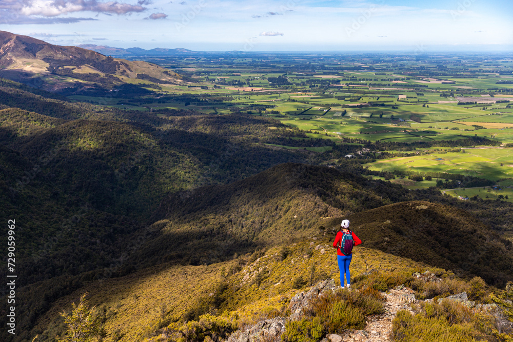Obraz premium hiker girl walking down the steep trail from the top of mount somers in canterbury, new zealand south island