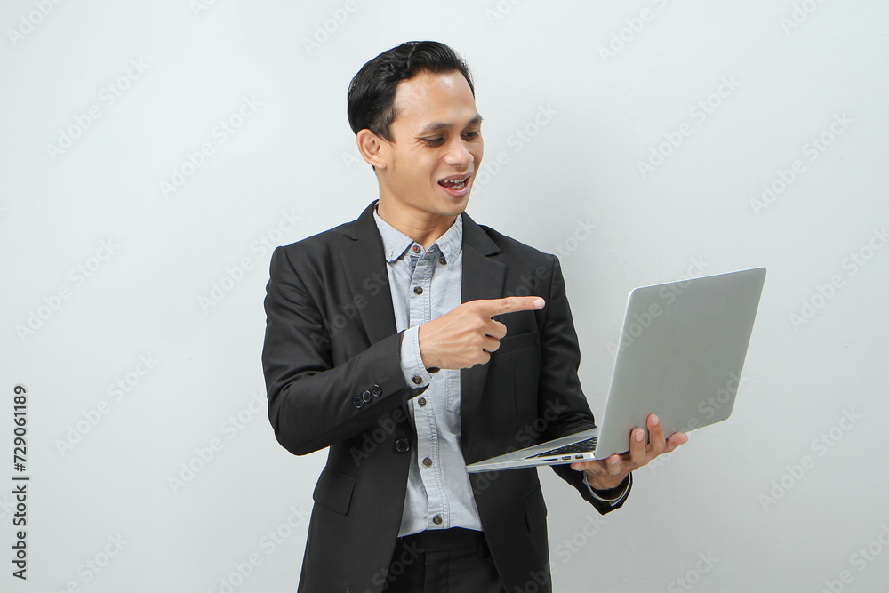 Happy asian indonesian business man in suit holding laptop computer with pointing finger gesture on isolated background Happy asian indonesian business man in suit holding laptop computer with pointing finger gesture on isolated background