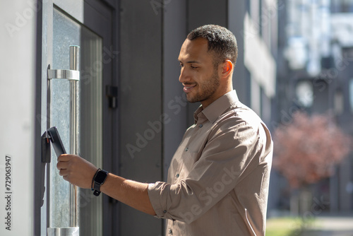 Side view of hispanic unshaved male opening entrance door with contactless plastic key card. Contemporary office worker electronic sensor for accessing building area only for authorized people.