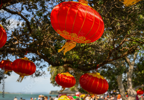 Red lanterns hanging under the Pohutukawa trees. Big crowd celebrating Chinese New Year at Mission Bay. Auckland.