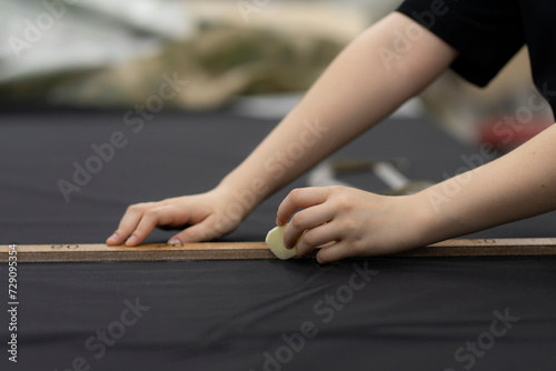 female tailor drawing a line with textile chalk in hand © Mihail