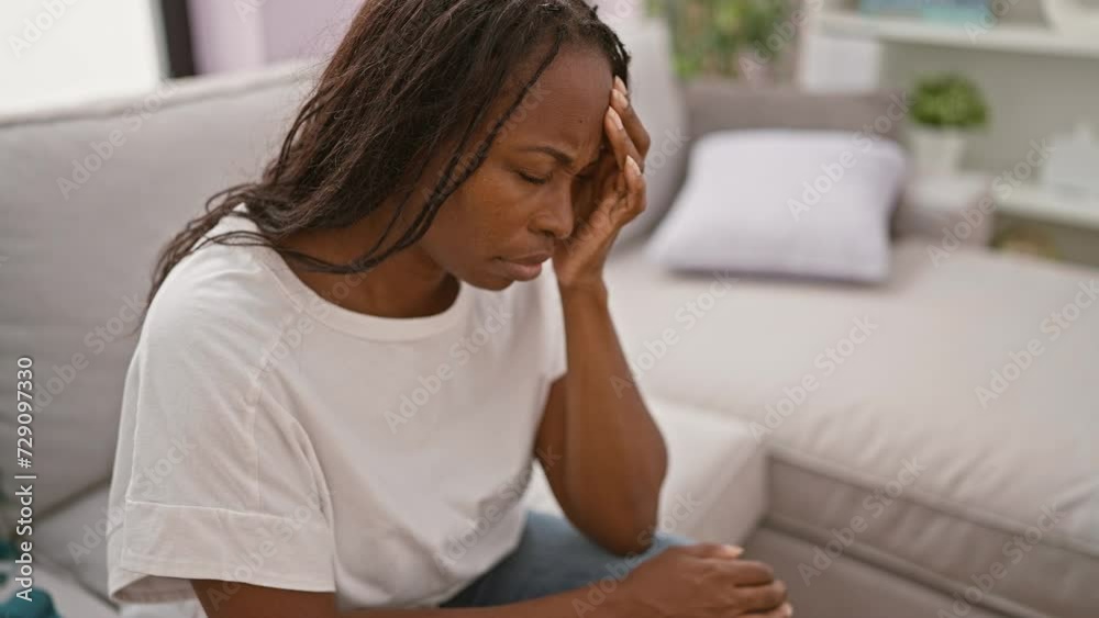 Stressed african american woman with curly hair sitting indoors at home, showcasing anxiety. Stressed african american woman with curly hair sitting indoors at home, showcasing anxiety.