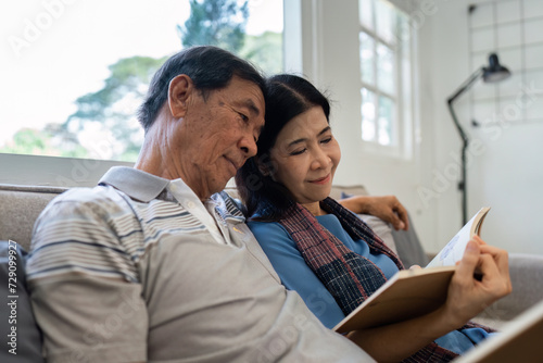 Retired elderly couple sits on couch in their home reading relaxing book. Senior Activity Concept