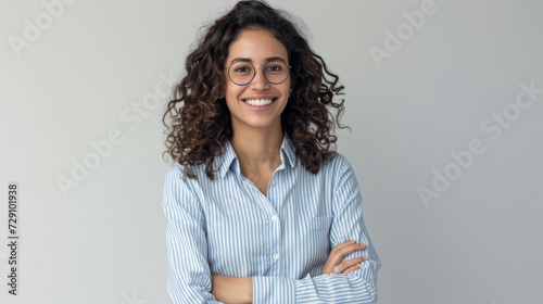 woman with short blonde hair and a confident smile is wearing a white shirt and stands with her arms crossed against a light grey background