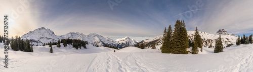 Panoramic view, Panorama view with snowy mountains in Bregenzerwald, Austria, Körber lake with brown Arlberg peak and river in snowfield, trees and sky with veil clouds