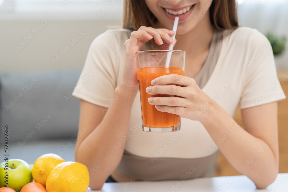 Orange detox juice concept, smile asian young woman hand holding a glass of vegetable juice, carrot smoothie for diet at home, drinking healthy meal food for weight loss. Lifestyle, vegan nutrition. Orange detox juice concept, smile asian young woman hand holding a glass of vegetable juice, carrot smoothie for diet at home, drinking healthy meal food for weight loss. Lifestyle, vegan nutrition.