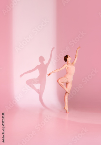 Pastel Pirouette. Young woman, ballerina dancer in pink ensemble poses against soft background. Her shadow dances in tandem. Concept of ballet, grace, beauty, harmony, shadowplay. Ad