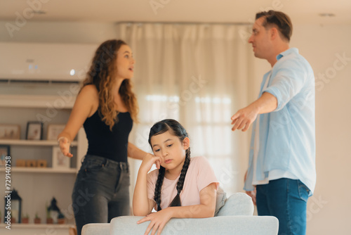 Annoyed and unhappy young girl sitting on sofa trapped in middle of tension by her parent argument in living room. Unhealthy domestic lifestyle and traumatic childhood develop to depression.Synchronos © Summit Art Creations