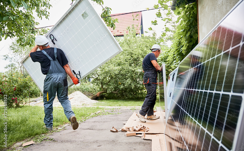Two men carrying solar modules in the yard. Male worker in safety ...