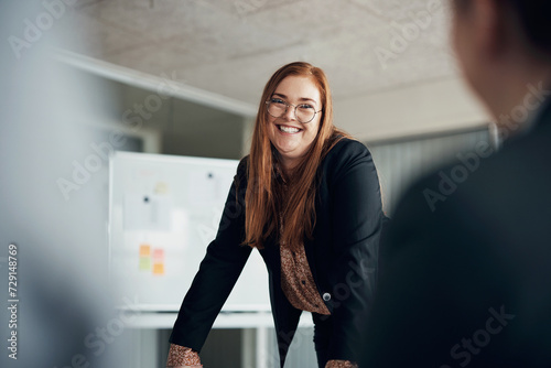 Young red head businesswoman laughing while giving a presentation to coworkers in an office photo