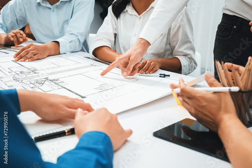 Diverse group of civil engineer and client working together on architectural project, reviewing construction plan and building blueprint at meeting table. Prudent photo