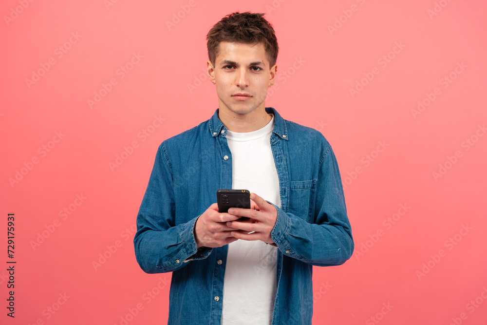 Portrait of serious man using mobile phone, texting on pink background looking at camera. Concept of human emotions, facial expression. Copy space for your ad Portrait of serious man using mobile phone, texting on pink background looking at camera. Concept of human emotions, facial expression. Copy space for your ad