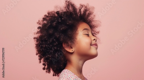 A young girl with curly hair closed eyes and a serene expression looking upwards against a soft pink background.