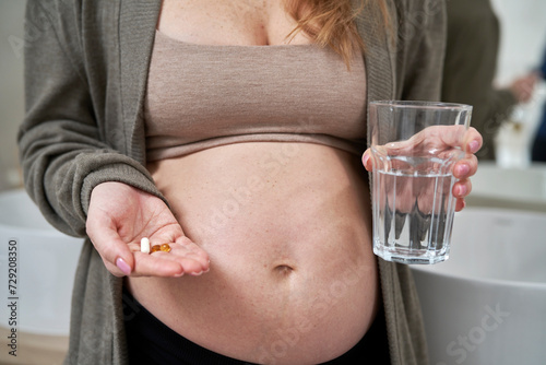 Caucasian pregnant woman holding nutritional supplements and a glass of water