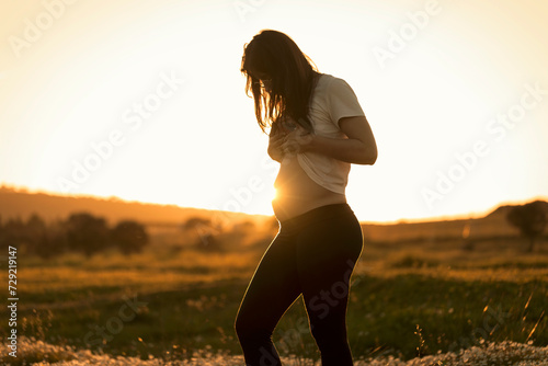 A pregnant woman looks at the sun reflecting on her belly against the light, waiting for the birth of the baby and her motherhood. Concept of giving birth pregnant and waiting for natural childbirth