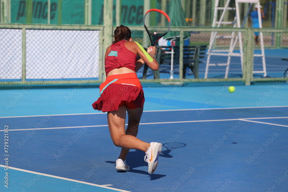 A girl plays tennis on a court with a hard blue surface on a summer sunny day	