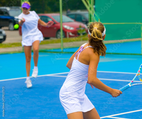 A girl plays tennis on a court with a hard blue surface on a summer sunny day 
