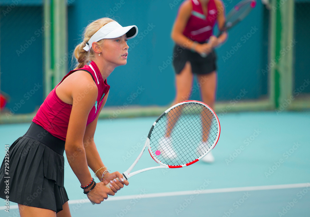A girl plays tennis on a court with a hard blue surface on a summer sunny da