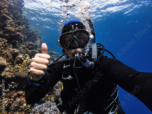 scuba diver makes GO UP sign, underwater scene with exotic fishes and coral reef