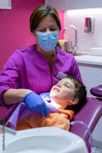 Female dentist putting disposable dental bib on a child at the dentist's office