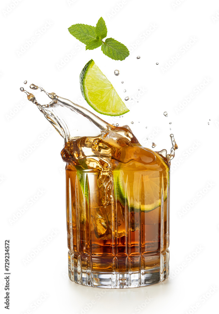 Lime wedge and mint falling into a splashing glass of rum and coke isolated on white background. Lime wedge and mint falling into a splashing glass of rum and coke isolated on white background.