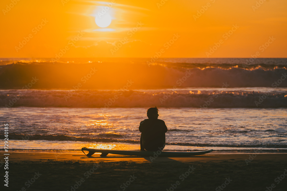 Silhouette of unrecognizable surfer sitting on surfboard at sunset by ocean Silhouette of unrecognizable surfer sitting on surfboard at sunset by ocean