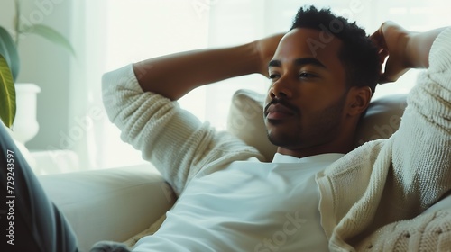 Candid millennial authentic diverse portrait of african american man relax time at apartment in neutrals tones interior.Domestic life multi ethnic male having thoughtful facial express : Generative AI