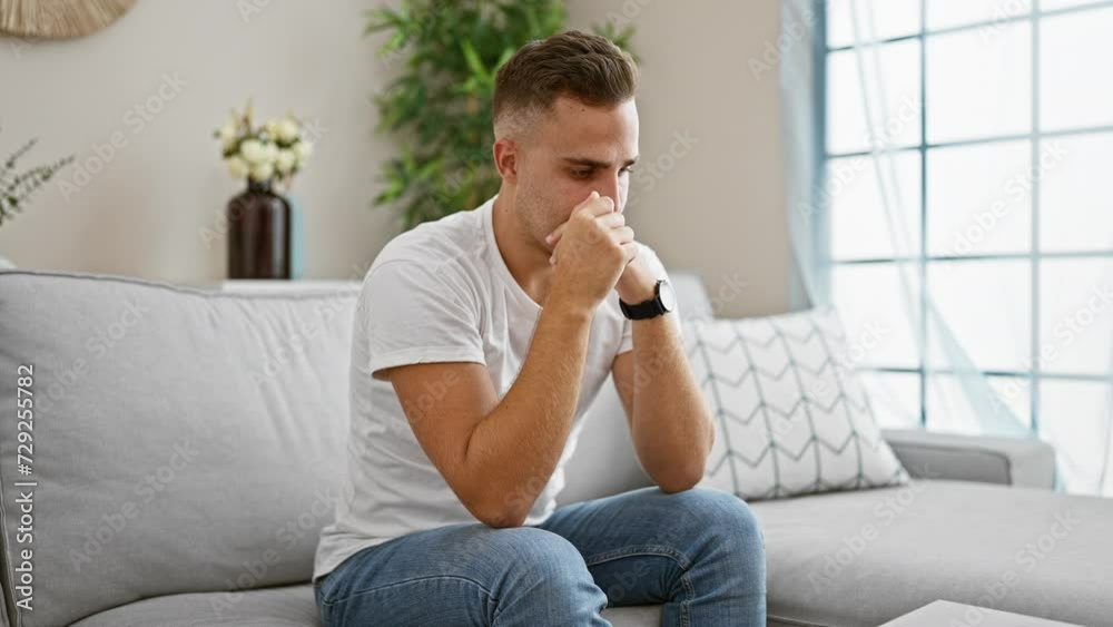 Pensive young man sitting in modern living room reflecting on thoughts. Pensive young man sitting in modern living room reflecting on thoughts.