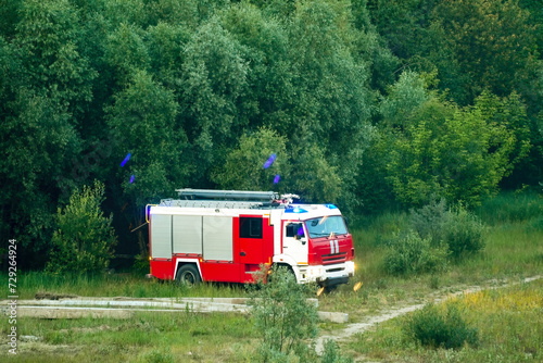 A fire truck with its lights on stands at the edge of the forest. Controlling the danger of forest fires.