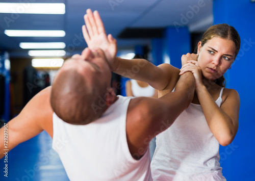 Young woman practicing basic self-defense techniques while training in gym with male partner, performing palm heel strike in chin