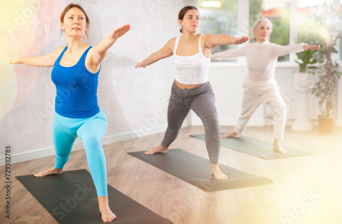 Active women who take care of their physical health and practice yoga in group training, perform the exercise in the warrior pose
