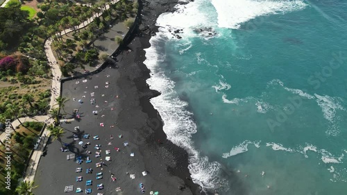 Aerial view of central beach in Puerto de la Cruz on the Canary Islands. Drone flying above Jardin beach. Beautiful black volcanic sand beach with palms and blue water.