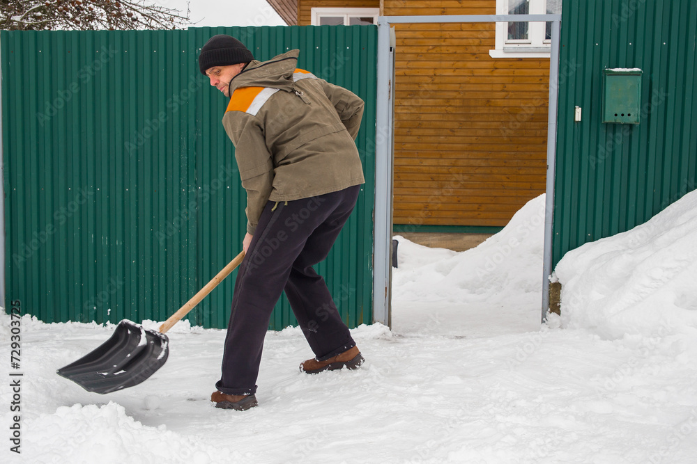 A European man removes snow near his house. A European man removes snow near his house.