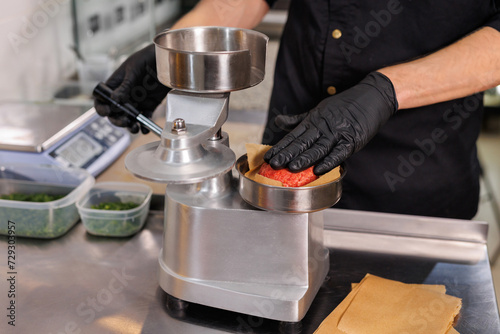 Canvastavla A cook using a press to make hamburger patties.