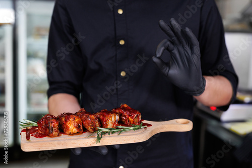 The cook holds a board with barbecue ribs and fresh rosemary in his hands.