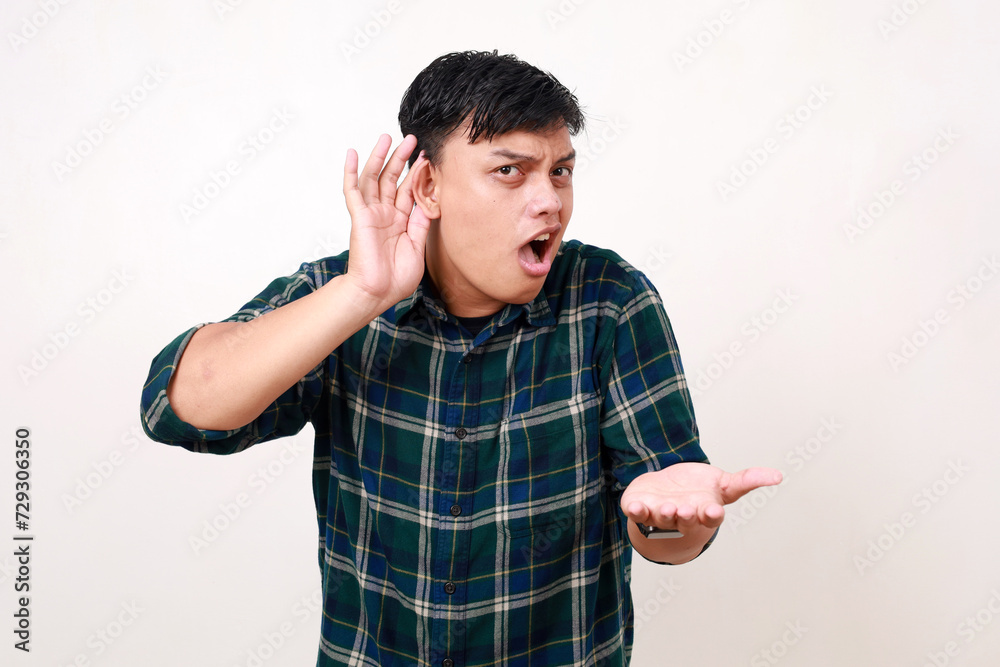 © ArvStd - I can’t hear you! Young asian man holding hand above ear asking to be louder over white background