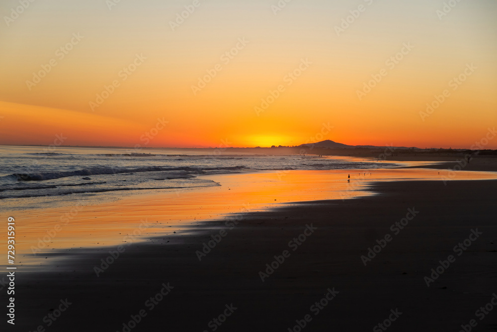 Sunset on beach at low tide with reflections of the orange sky in the water, The Algarve, Portugal