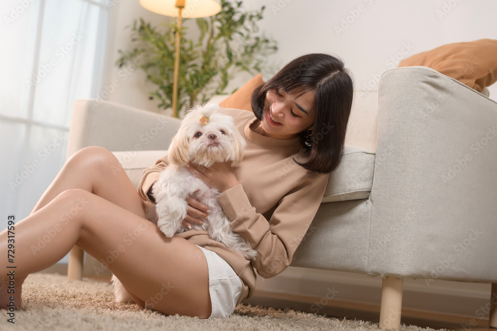 Happy young asian woman cuddling and spending time with cute dog in living room.
