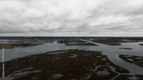 An aerial view over the salt marsh off Freeport, New York on a cloudy day. The drone camera dolly in and slowly tilt downwards, high up over the waters and brown marsh grass, heading towards land. photo