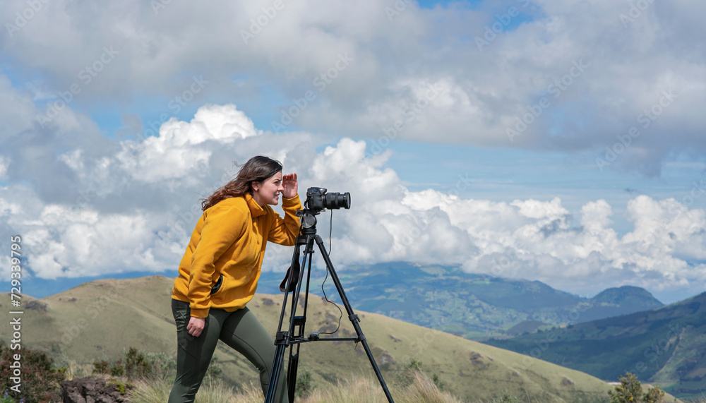 Beautiful young Latin American woman with her camera and tripod taking photos of landscapes on the top of a mountain