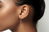  Close-up photo of a minimalist silver hoop earring in a woman's ear, with light skin tone