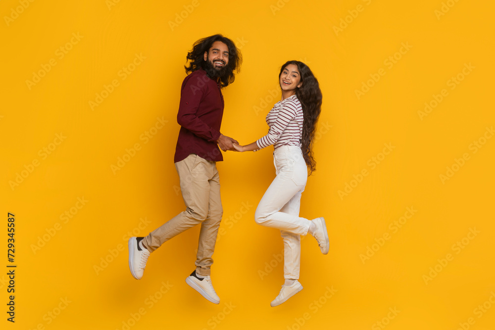 Positive carefree indian man and woman holding hands, jumping