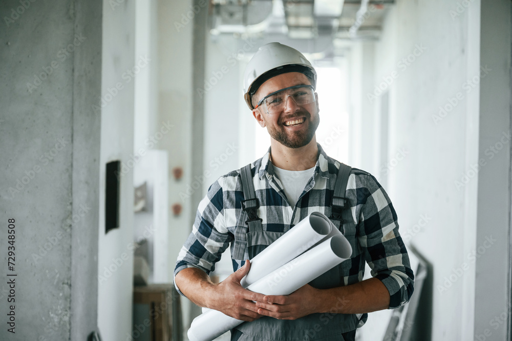 Positive smiling construction worker in uniform in empty unfinished room Positive smiling construction worker in uniform in empty unfinished room