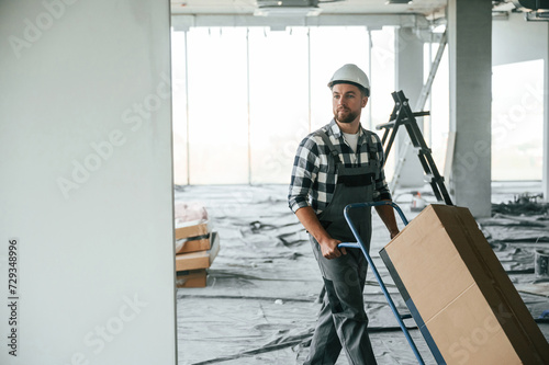 With large box, transporting the material. Construction worker in uniform in empty unfinished room