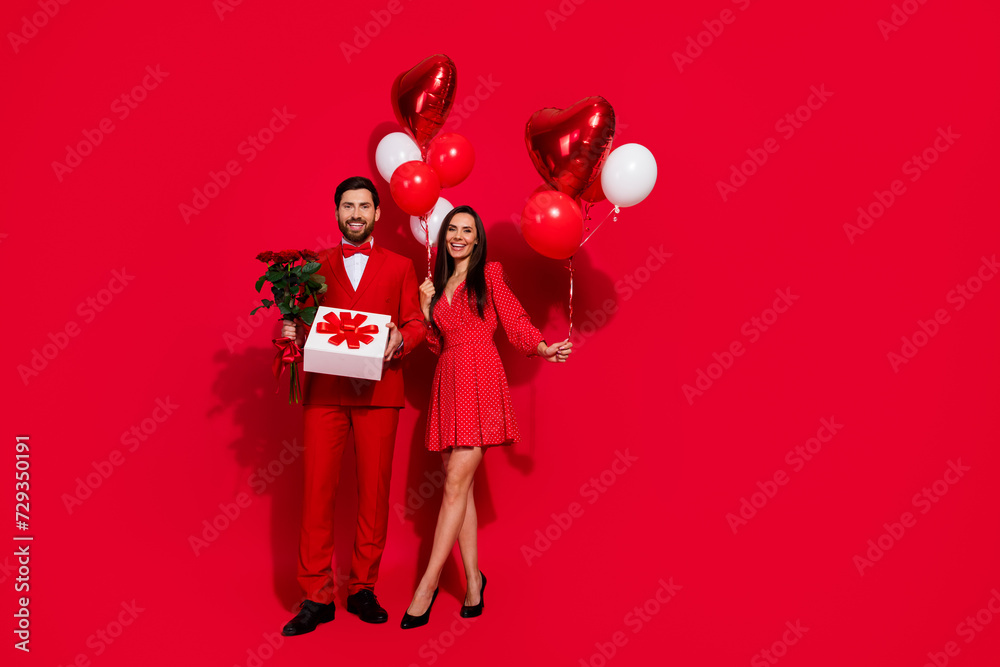 Full length photo of stunning young couple present celebration valentine day wear trendy elegant garment isolated on red color background Full length photo of stunning young couple present celebration valentine day wear trendy elegant garment isolated on red color background