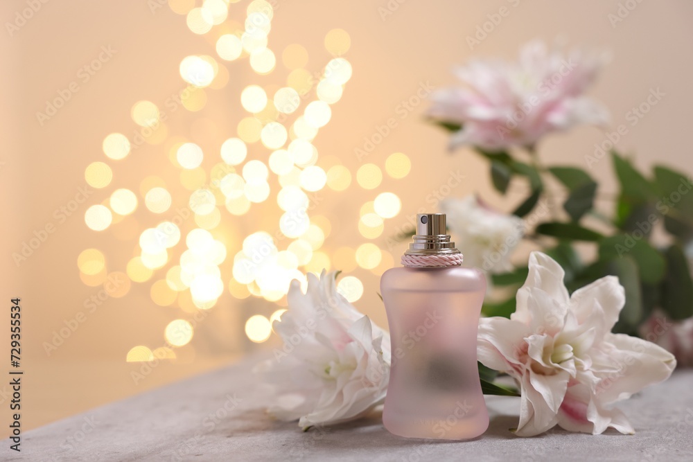 Bottle of perfume and beautiful lily flowers on table against beige background with blurred lights, closeup. Space for text Bottle of perfume and beautiful lily flowers on table against beige background with blurred lights, closeup. Space for text