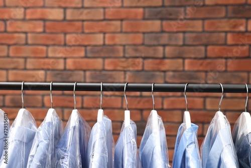 Dry-cleaning service. Many different clothes hanging on rack against brick wall, space for text