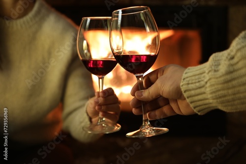 Couple clinking glasses of wine near fireplace at home, closeup